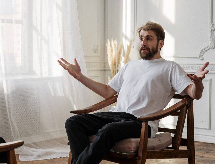man in white crew neck t shirt sitting on brown wooden rocking chair