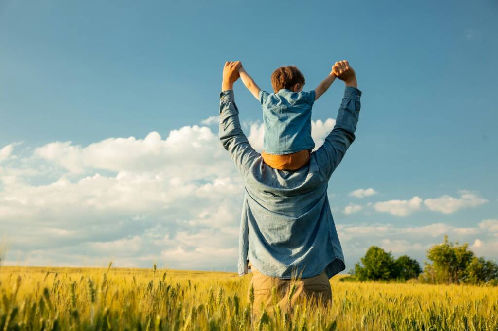 father and son in wheat field, child sitting on his fathers shoulders